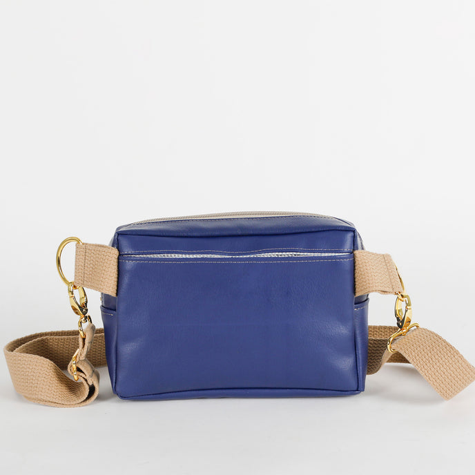The back of this southwest blue bag with a pocket and a  beige strap on a light gray background