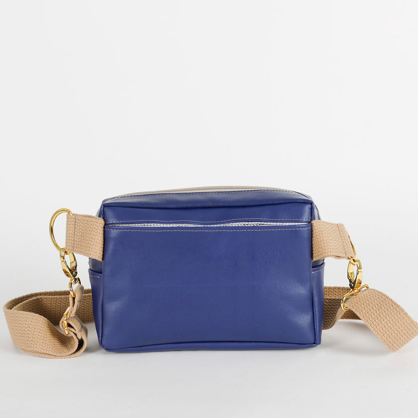 The back of this southwest blue bag with a pocket and a  beige strap on a light gray background