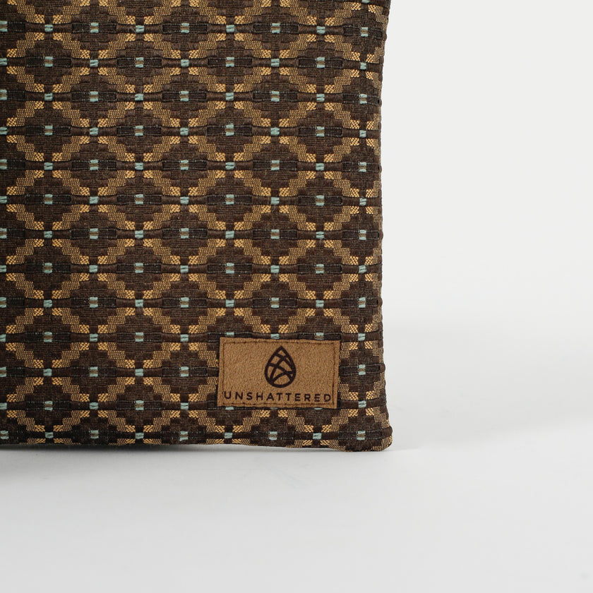 Close up of a brown ultrasuede Unshattered label on a brown and blue geometric print fabric crossbody pouch