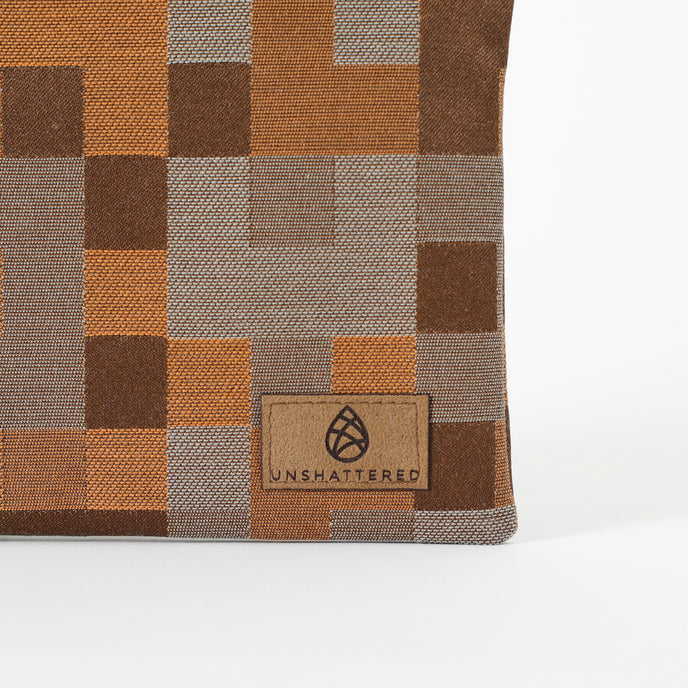 Close up of a brown suede, Unshattered label on a pouch with a modern geometric square pattern in various shades of brown. 