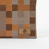 Close up of a brown suede, Unshattered label on a pouch with a modern geometric square pattern in various shades of brown. 