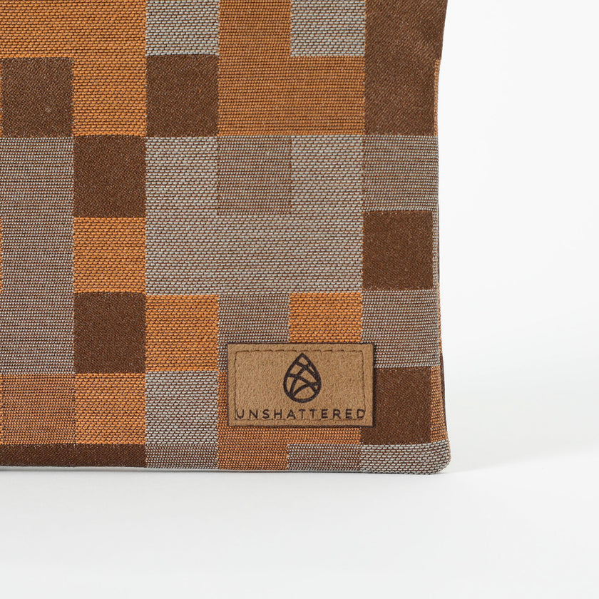 Close up of a brown suede, Unshattered label on a pouch with a modern geometric square pattern in various shades of brown. 