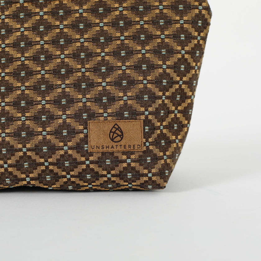 Close up of a brown, ultrasuede Unshattered label on a makeup bag with a brown and blue geometric pattern