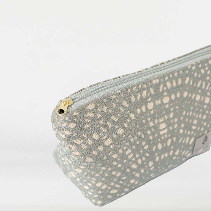 A gray fabric with circles pattern on a makeup bag with gold toned zipper named after Abby