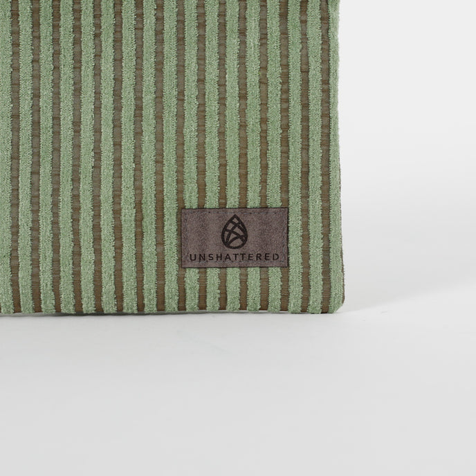 Close up of a gray, ultra-suede Unshattered label on a green plush zippered pouch