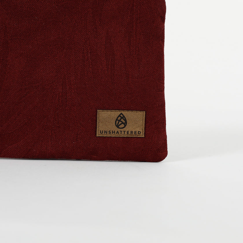 Close up of a brown, ultrasuede Unshattered label on a burgundy floral damask fabric pouch 