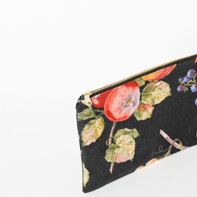 A gold toned zipper on a black fruit design fabric large zip pouch named after Diane