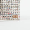 A tan label on a tweed multi-color crossbody pouch named after Lydia