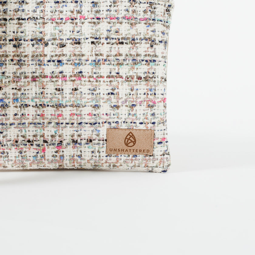 A tan label on a tweed multi-color crossbody pouch named after Lydia