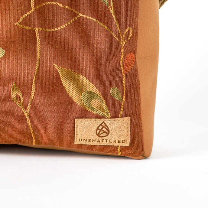 Brown fabric with leaf patterns and 'Unshattered' brand label on a white background named after Nita 