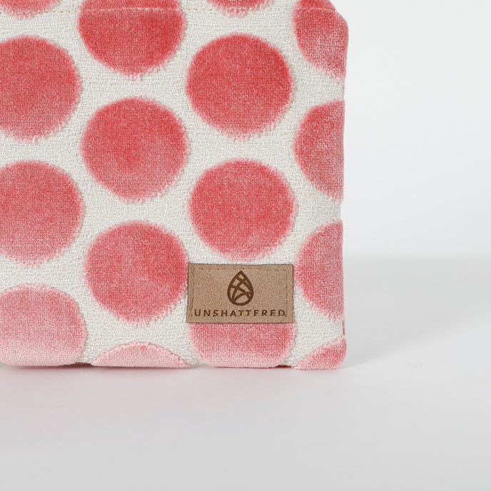 Fabric with pink polka dots and a Unshattered tan label on a white background