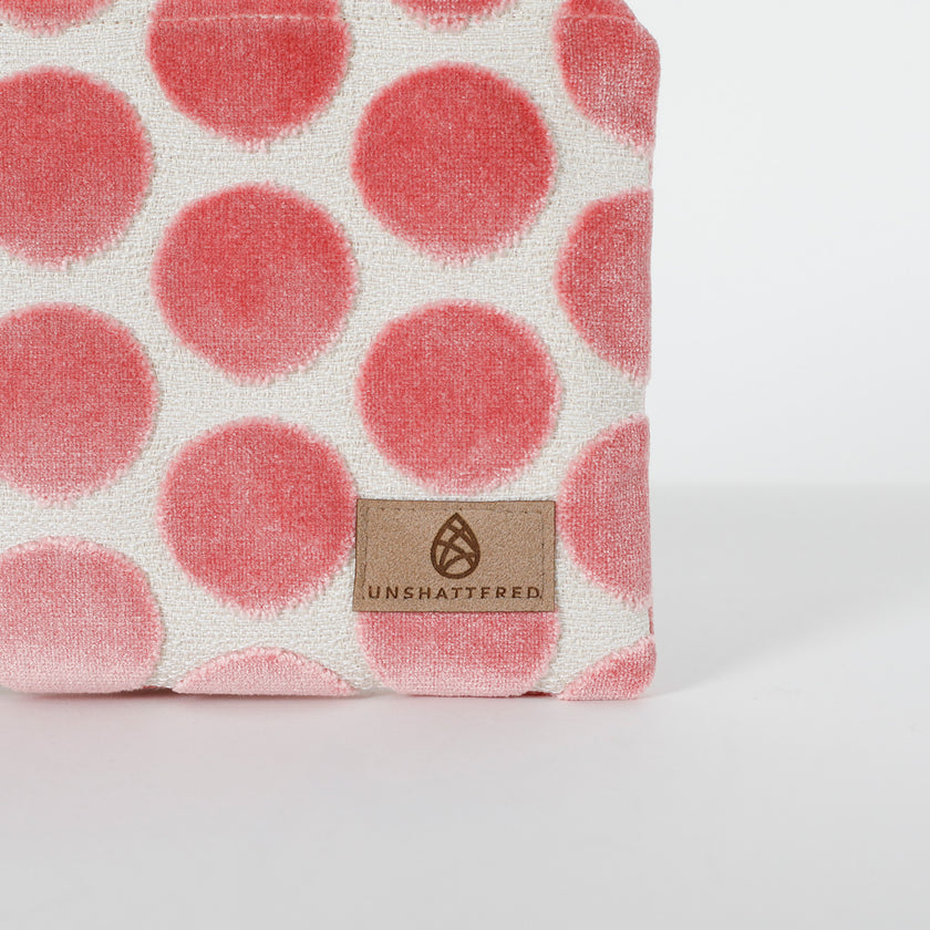 Fabric with pink polka dots and a Unshattered tan label on a white background