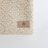 Textile with a beige and white pattern and 'Unshattered' brand label on a white background