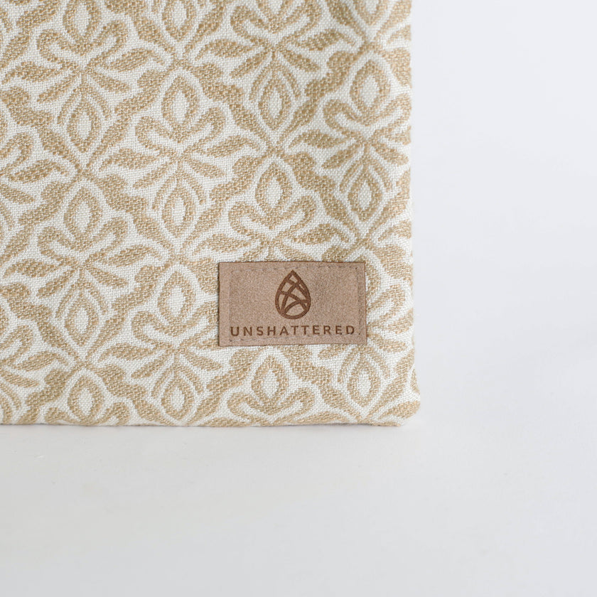 Textile with a beige and white pattern and 'Unshattered' brand label on a white background