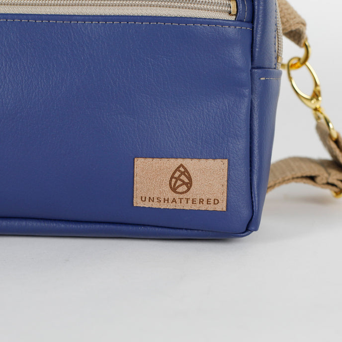 Blue Southwest leather bag with 'Unshattered' brand logo on a light gray background