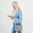 A woman handsfree wearing a silver and gray dotted Maggie crossbody pouch with an adjustable strap and a zipper closure, handcrafted from upcycled materials.