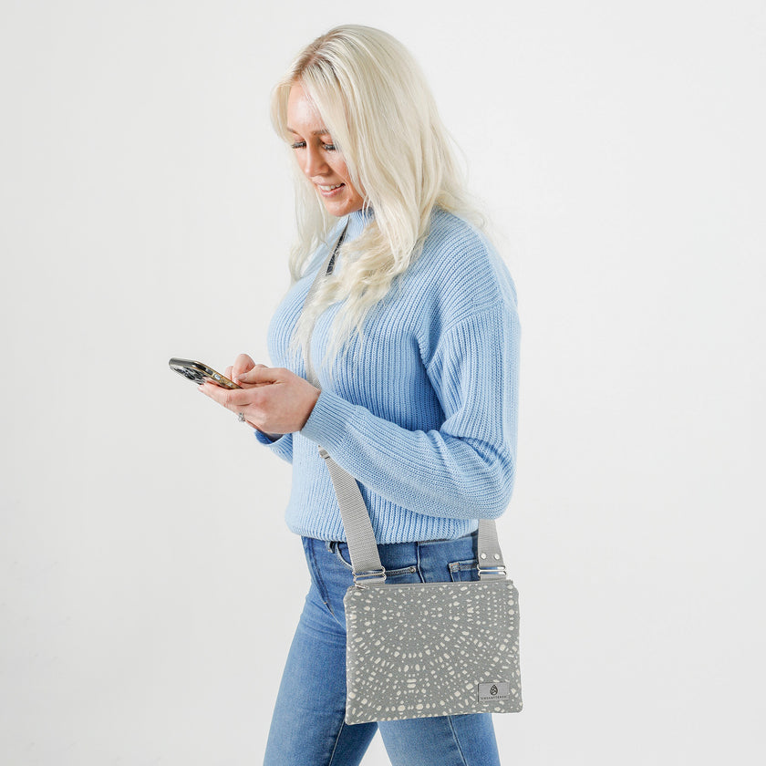 A woman handsfree wearing a silver and gray dotted Maggie crossbody pouch with an adjustable strap and a zipper closure, handcrafted from upcycled materials.