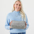 A woman wearing a blue sweater holding a gray spotted Haley toiletry kit with a geometric pattern, featuring a zip closure and a gray fabric lining.
