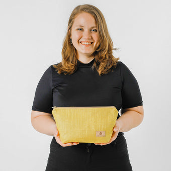 A woman holding a small, chartreuse yellow makeup kit with a zip closure, made from upcycled fabric, named after Madison