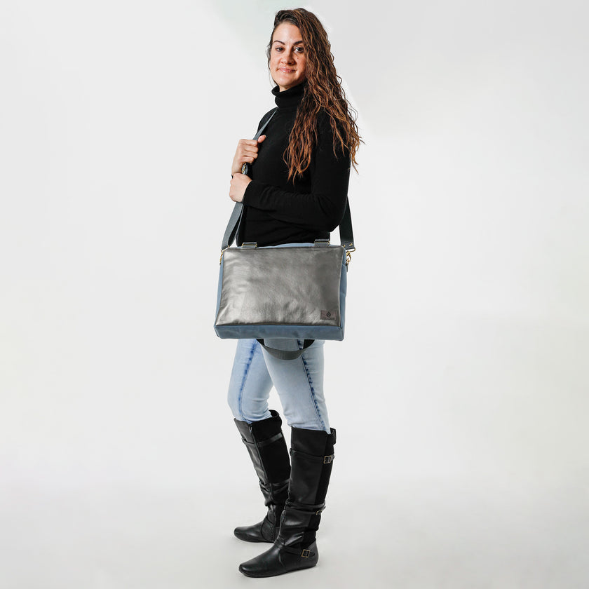 A woman holding a charcoal luxury leather alternative handbag with gray straps and gold tone hardware on a white background named after Wanda.