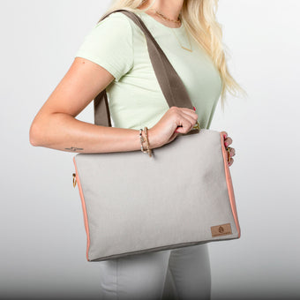 A woman carrying a tan outdoor furniture material on the exterior with brown straps and gold hardware coral peach luxury leather alternative accents 