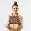 A woman holding a zippered pouch with a modern geometric square pattern in various shades of brown named after Jazzmaine.