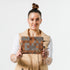 A woman holding a zippered pouch with a modern geometric square pattern in various shades of brown named after Jazzmaine.