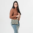 Woman holding an green, ivy patterned fabric crossbody pouch against a plain background