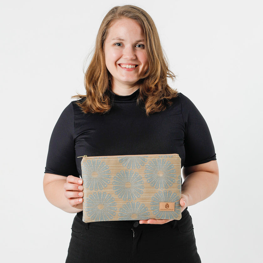 A woman holding a large zip pouch with a warm tan base and vibrant blue flower pattern, featuring a gold-tone zipper  named after Sherry on the bottom right.