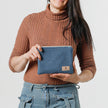 A woman holding a small zip pouch with blue paisley fabric and gold-tone hardware, featuring a brand tag that reads Unshattered named after Shiera