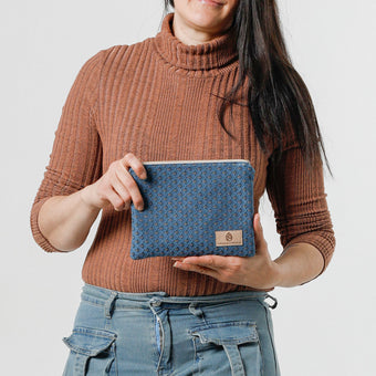 A woman holding a small zip pouch with blue paisley fabric and gold-tone hardware, featuring a brand tag that reads Unshattered named after Shiera
