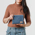A woman holding a small zip pouch with blue paisley fabric and gold-tone hardware, featuring a brand tag that reads Unshattered named after Shiera