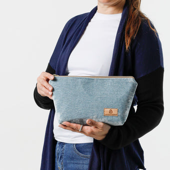 A woman holding a  blue makeup kit with a velvety exterior, a wipe-clean interior, and a secure zip closure, handcrafted from upcycled materials named after Kimberly