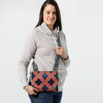 A woman carrying a red and blue embossed crossbody pouch with an adjustable strap and zipper closure named after Samantha.
