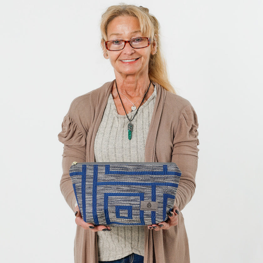 A woman holding a makeup bag with a geometric pattern in blue and gray tones and a zippered closure named after Teresa.