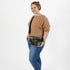 A woman wearing a tan sweater while carrying a woodland camo errand bag with black straps and black metal hardware 