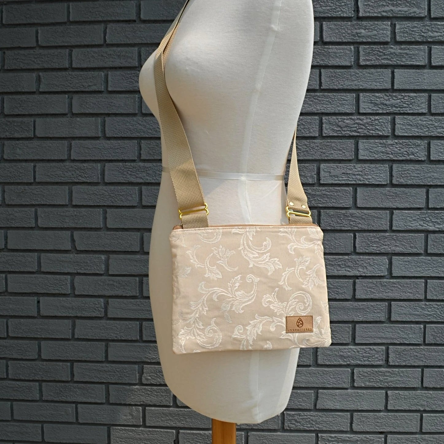 One cream bag with a floral design hanging on a mannequin in front of a gray brick wall. 