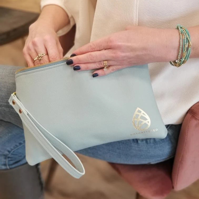 Kelly Lyndgaard holding a limited edition leather zip wristlet as she sits on a chair.