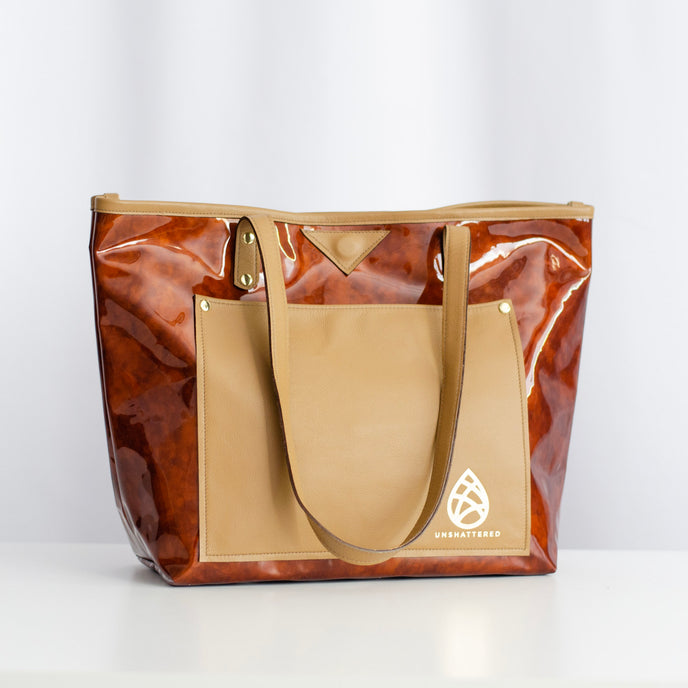 A brown and tan leather tote bag with gold-tone hardware and two leather shoulder straps, displayed against a neutral background.