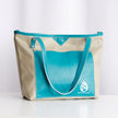 A leather tote bag with pebble-colored body and cerulean-colored trim, featuring two shoulder straps and a logo on the side.