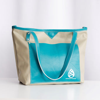 A leather tote bag with pebble-colored body and cerulean-colored trim, featuring two shoulder straps and a logo on the side.