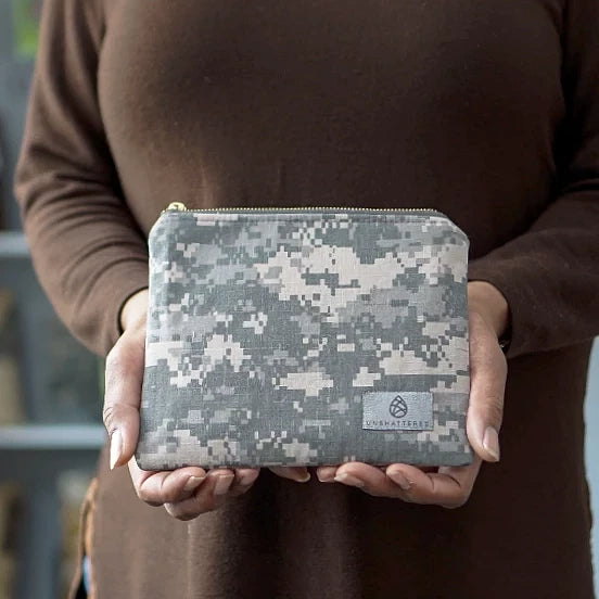 Woman holding a small zip pouch with an army digital camouflage pattern, featuring a gray label and gold-tone hardware.